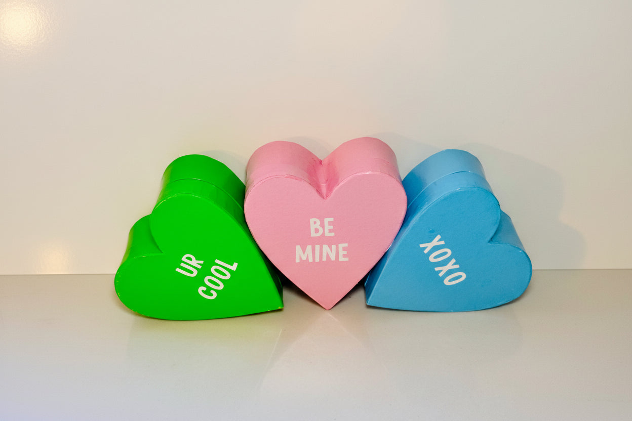 Three heart-shaped boxes in green, pink, and blue with printed messages on a white background.